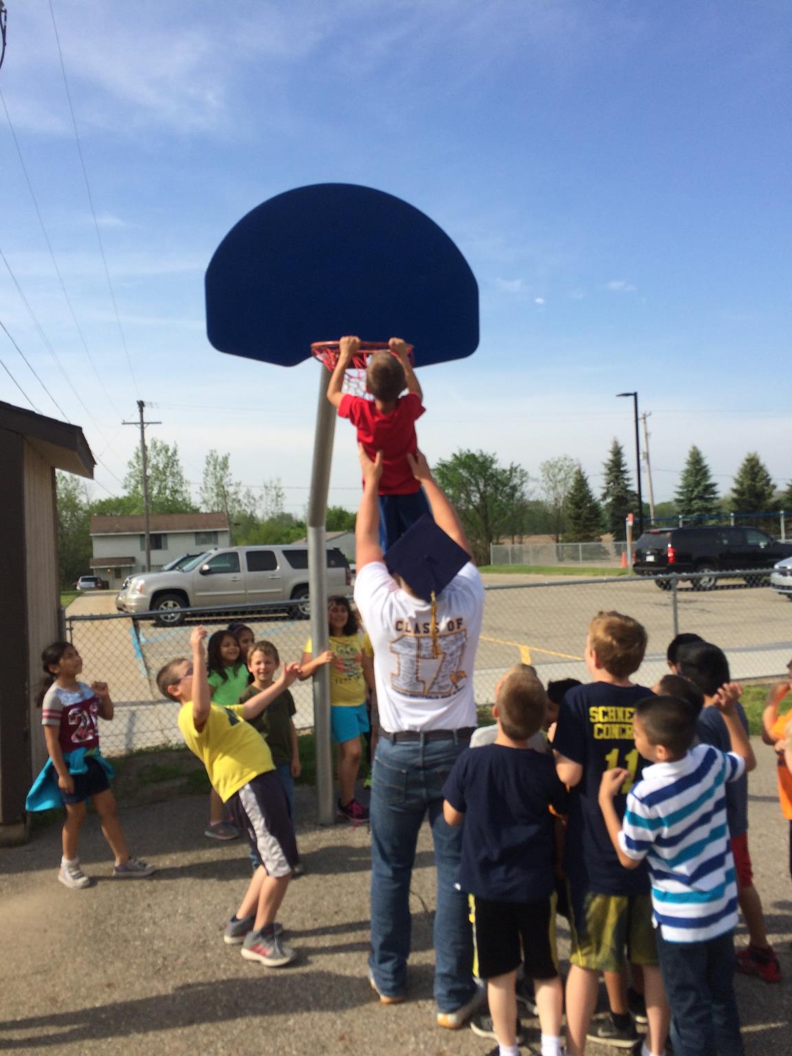 A member of the Class fo 2017 hoists up a Pewamo Elementary School student to dunk a basket ball on the playground during their visit on their last day before becoming PW graduates.