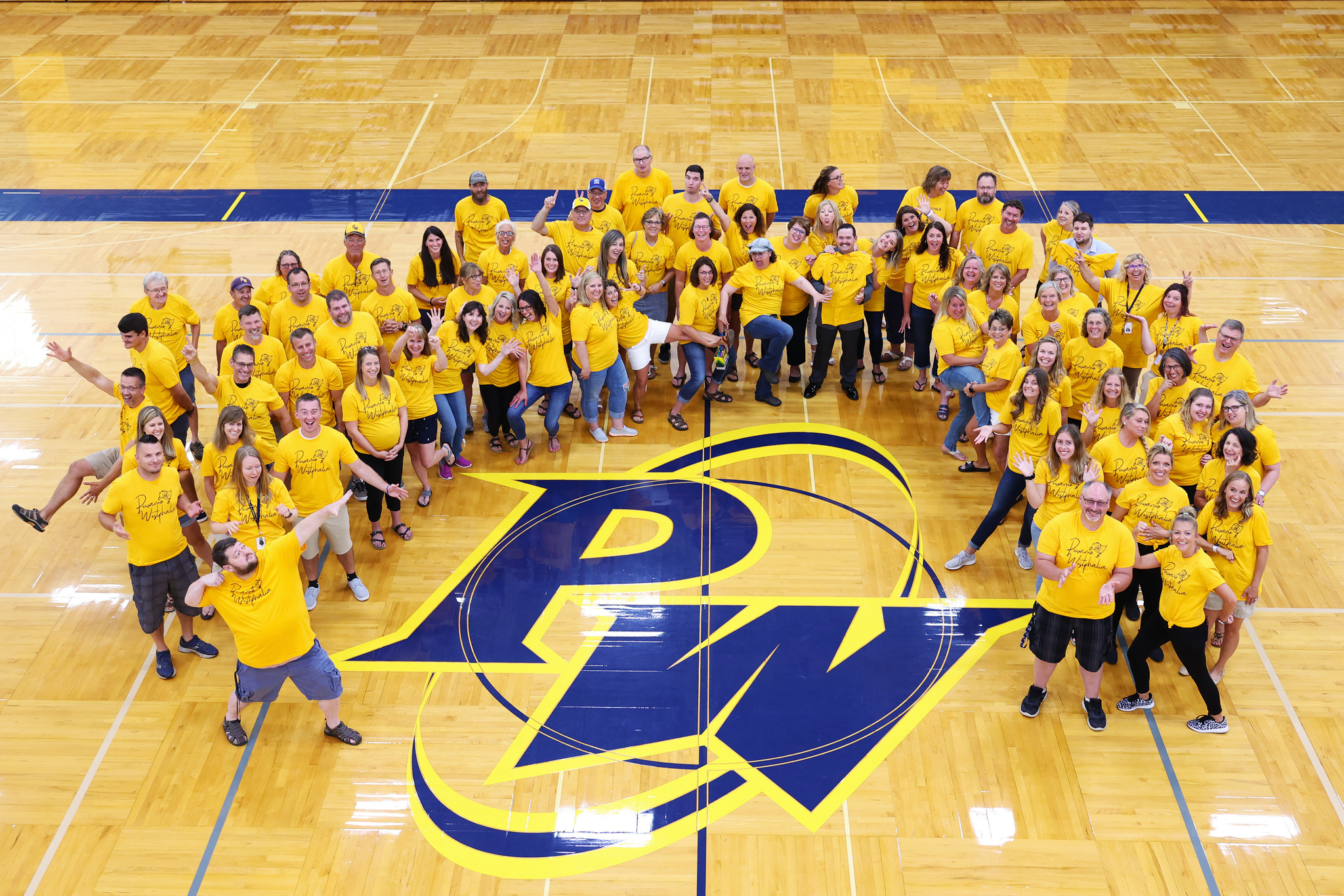 Staff of PW Schools in yellow shirts on a gymnasium floor